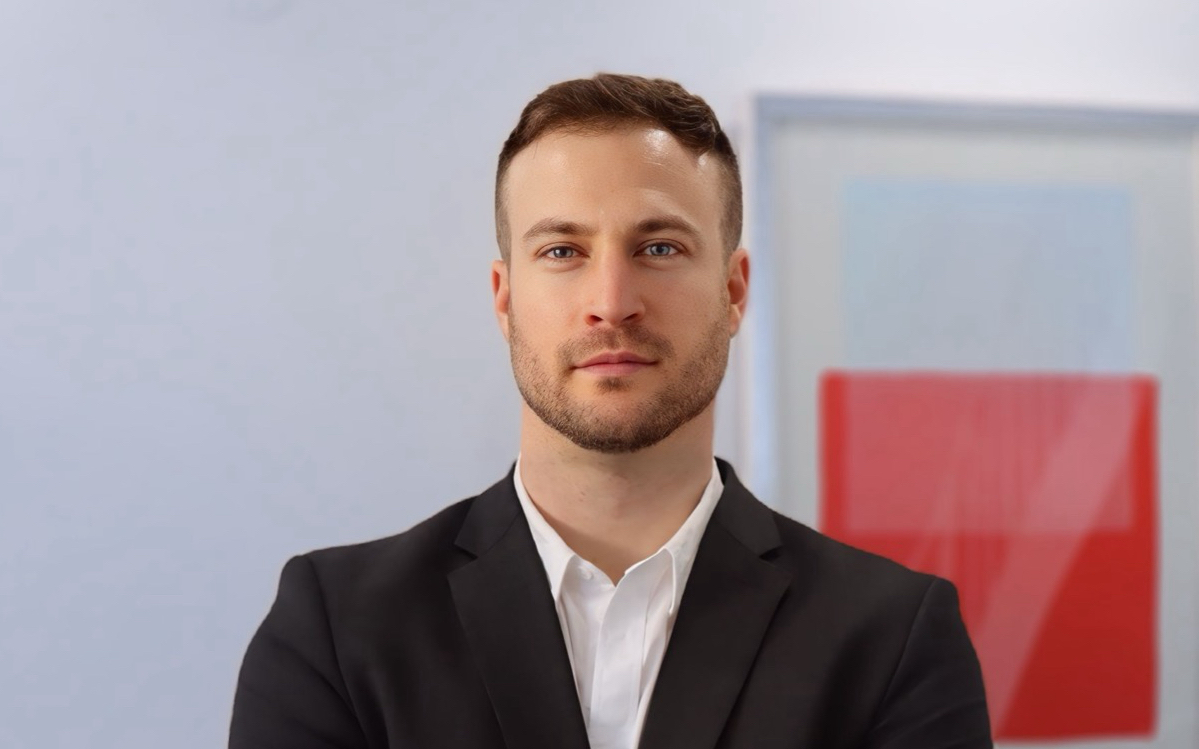 Porträt eines jungen Mannes namens Marvin Krämer in einem schwarzen Anzug mit weißem Hemd, der vor einem modernen Hintergrund mit abstrakter Kunst posiert.