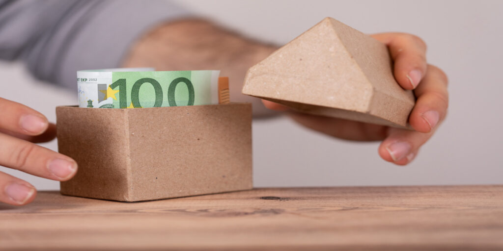 Symbol für Immobilienfinanzierung: Ein Papphaus mit einem Geldschein darin.