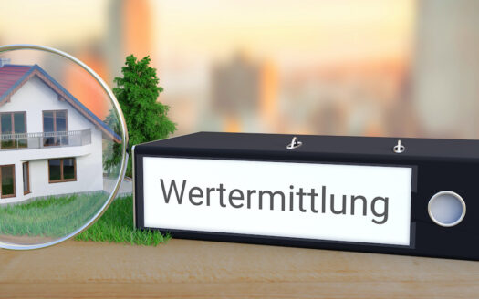 Wert einer Immobilie. Akten-Ordner beschriftet mit dem Wort Wertermittlung liegt neben einem Haus-Modell mit Lupe auf einem Schreibtisch. Skyline einer Stadt im Hintergrund. Der Wert einer Immobilie. Ein Aktenordner, auf dem das Wort steht.